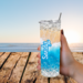 Woman holding sandy beach tumbler outdoors atthe beach  with wood table – calm beach vibes anywhere you go.

